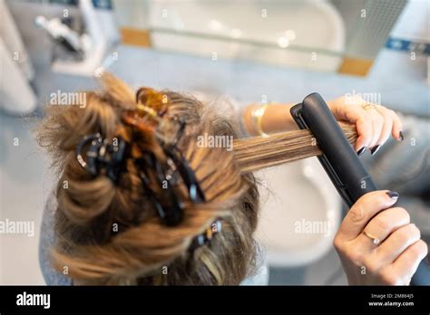 Blonde Woman Ironing Her Hair With An Electrical Appliance In The Bathroom Top View Stock Photo