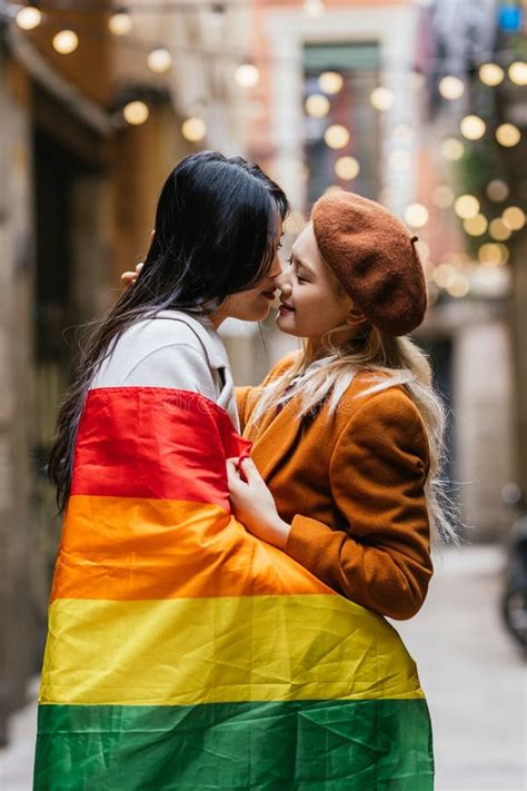 Lesbian Couple Kissing While Wrapped In Lgbt Rainbow Flag Outdoors On