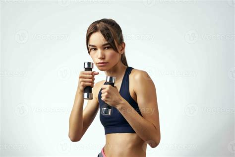 athlétique brunette avec haltères dans sa mains svelte figure Gym lumière Contexte 23656391