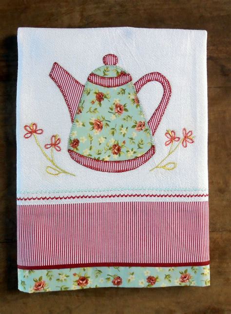 An Embroidered Teapot On A White And Pink Striped Napkin With Red Trim