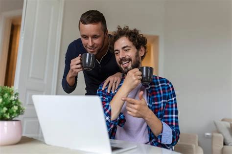 Lindo casal gay rindo juntos enquanto está sentado em sua sala de estar em casa dois românticos