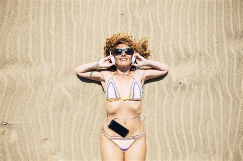 Vista Superior De La Mujer Joven En Bikini Tumbado En La Arena Tomando El Sol Mientras Escucha