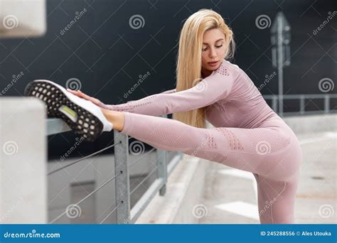 Beautiful Sporty Blonde Girl With Slim Body In Fashion Pink Sportswear Doing Leg Stretching And