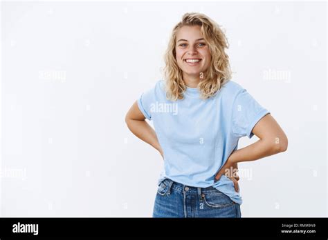 Fröhlich und optimistisch Süß lächelnde blonde Mädchen mit lockigem Haar Hände auf Taille