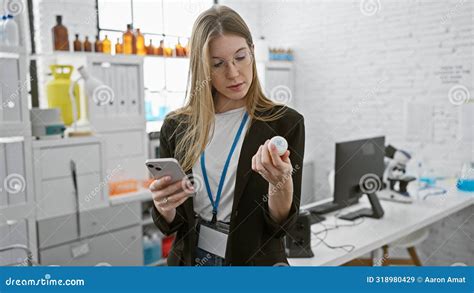 Blonde Woman Examines Medication While Holding Smartphone In A Laboratory Stock Image Image Of
