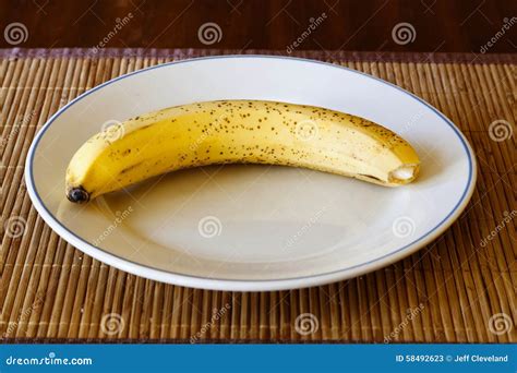 Single Banana With Some Brown Ripening Spots On Plate Stock Image