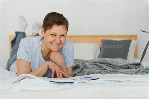 Middle Age Blonde Woman Reading Book Lying On The Bed At Home Stock Photo At Vecteezy