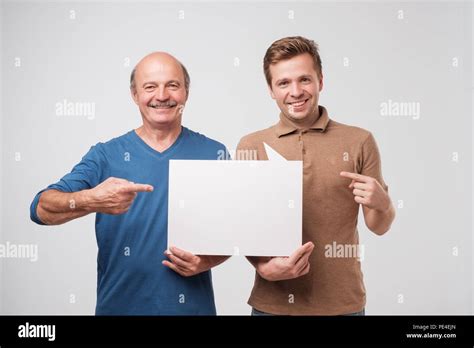 Two Mature Men Father And Son Are Holding A White Empty Billboard Together The Friends Are