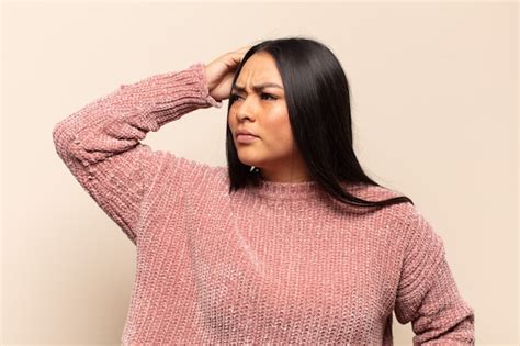 Mujer latina joven que se siente perpleja y confundida rascándose la cabeza y mirando hacia un