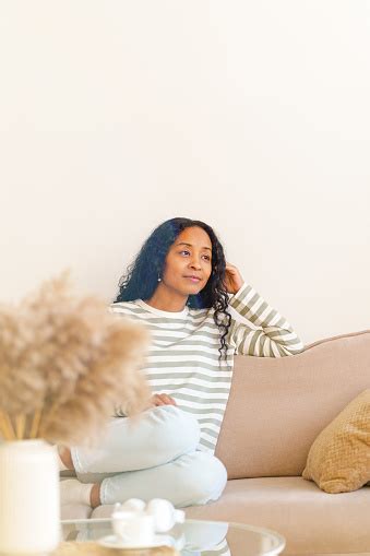 사려 깊은 아프리카 계 미국인 여성이 거실의 소파에 앉아 꿈을 꾸고 선택적인 초점을 맞 춥니 다 35 39세에 대한 스톡 사진