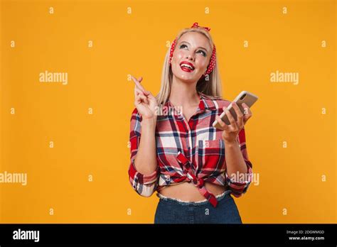 Image Of Joyful Blonde Pinup Girl Holding Fingers Crossed While Using Cellphone Isolated Over