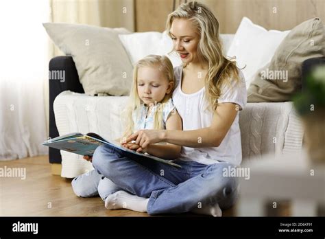 Bonne famille Une jeune mère blonde lit un livre à sa jolie fille tout en étant assise au sol