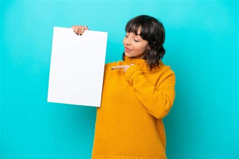 Jovem mulher latina isolada em fundo azul segurando um cartaz vazio expressão feliz e