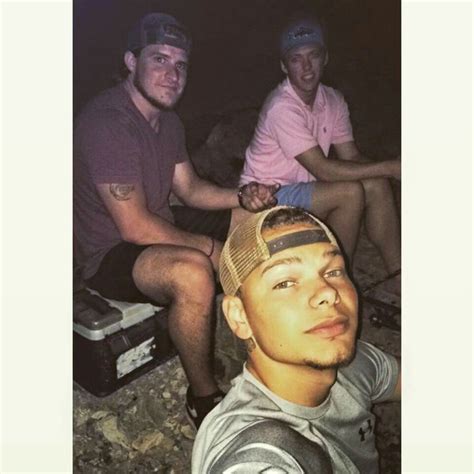 Three Men Sitting Next To Each Other In Front Of A Rock Wall And One Is