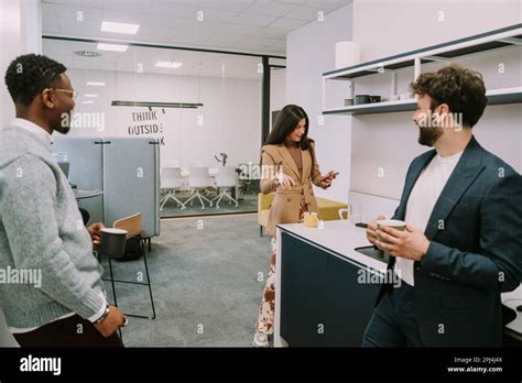 Two Diverse Male Colleagues Listening To Their Female Brunette Coworker Reading Something Funny
