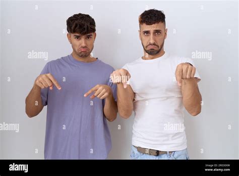 Homosexual Gay Couple Standing Over White Background Pointing Down Looking Sad And Upset