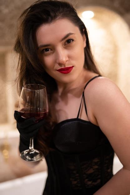 Linda garota em lingerie erótica sentada no banheiro uma taça de vinho Foto Premium