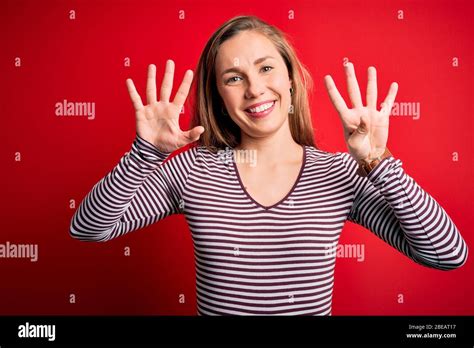 Junge schöne blonde Frau mit legeren gestreiften T Shirts über isoliertem rotem Hintergrund