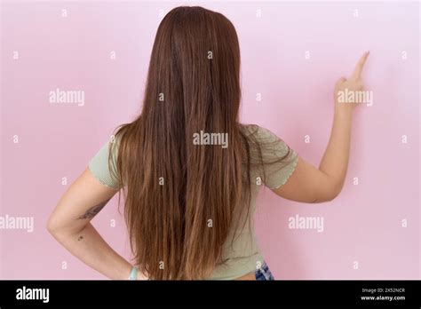 Beautiful Brunette Woman Standing Over Pink Background Posing Backwards Pointing Ahead With