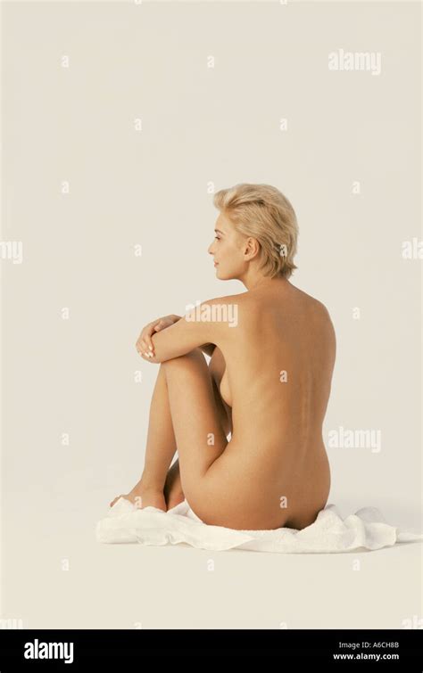 Side View Of Blond Nude Blond Woman With Short Hair Seated On White Towel On Floor In Studio