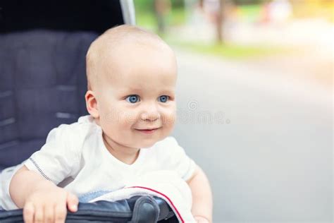 De Leuke Kaukasische Blonde Nieuwsgierige Zitting Van De Babyjongen In Wandelwagen Glimlachend