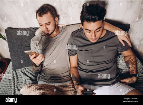 Happy Gay Couple Lying Together In Bed And Using Smartphone Looking At Photos Stock Photo Alamy