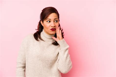 La mujer latina de mediana edad aislada en una pared rosa está diciendo una noticia secreta de