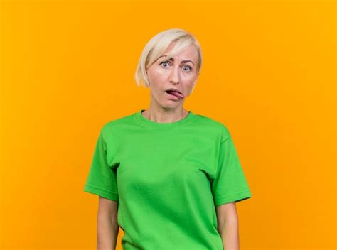 Ludique D âge Moyen Blonde Femme Slave Regardant Avant Montrant La Langue Isolée Sur Mur Jaune