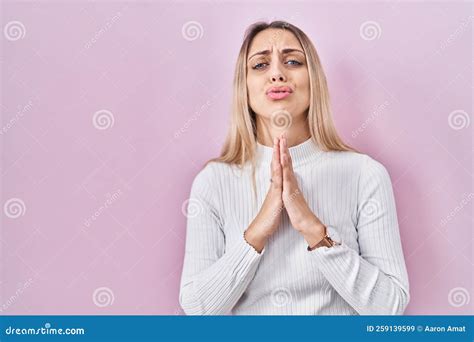 Ragazza Bionda Con Un Maglione Bianco Su Sfondo Rosa Mendica E Prega A Mani Nude Con La Speranza