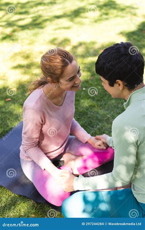 Happy Biracial Lesbian Couple Practicing Yoga Sitting Holding Hands And Smiling In Sunny Garden