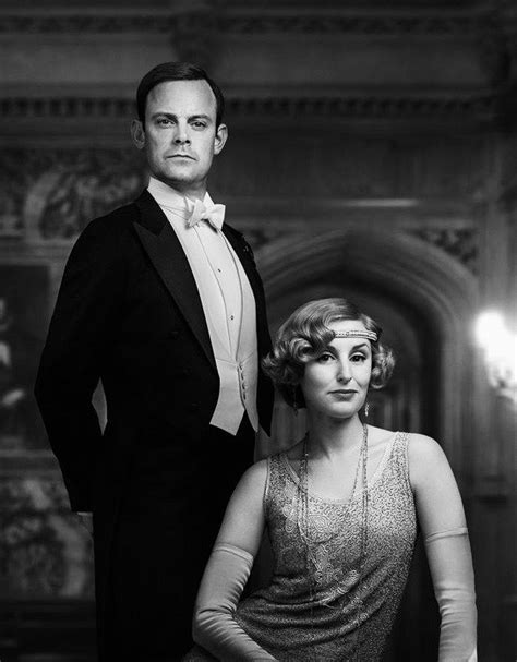 a man in a tuxedo standing next to a woman wearing a dress and necklace