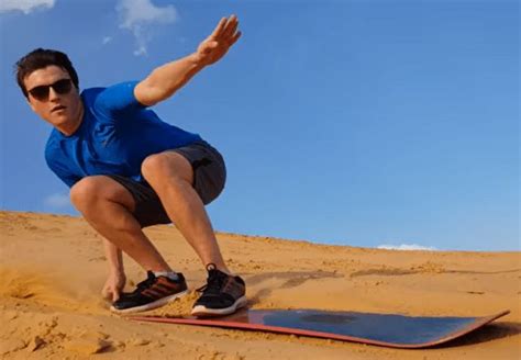 a man kneeling down on top of a surfboard in the sand with his hand out