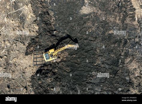 Yellow Working Excavator Digging Black Soil Or Peat Aerial Top View