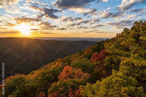 Sun setting behind clouds illuminating the fall colors of the trees in ...