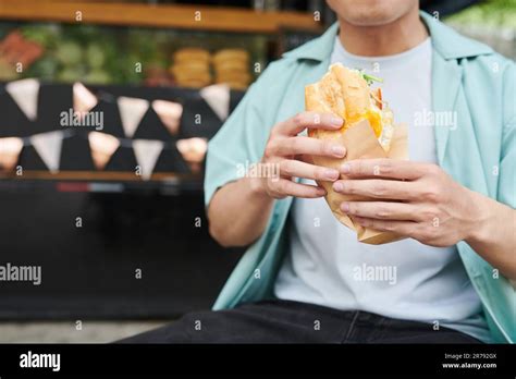 Gros plan sur un jeune homme affamé en tenue décontractée tenant un hot dog appétissant en