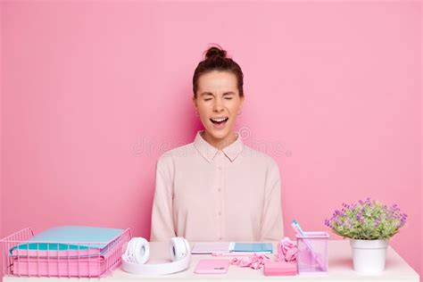 Brunette Woman Screams With Eyes Closed Seats At The Working Desk Isolated Next To The Pink