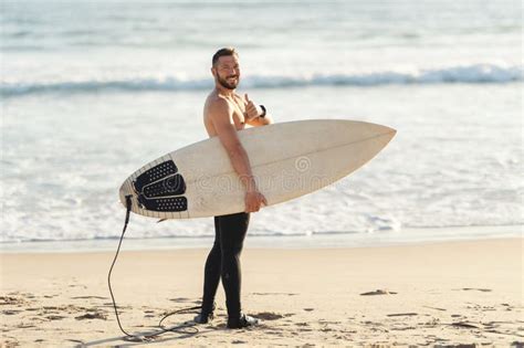 An Athletic Man Surfer With Naked Torso Standing By The Sea And Showing A Thumb Up Looking In