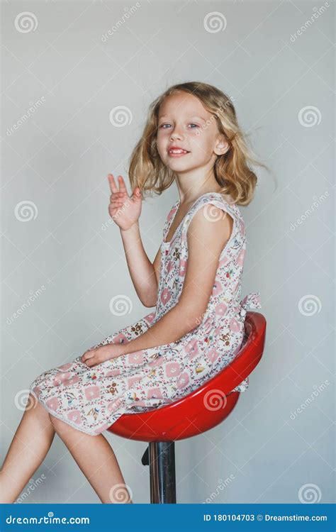 Jeune Fille Européenne Mignonne Sur Fond Gris Assise Sur Une Chaise Rouge Belle Blonde Bouclés