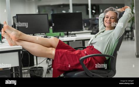 Mature Caucasian Woman Took Off Her Shoes And Put Her Feet On The Desktop In The Office Stock