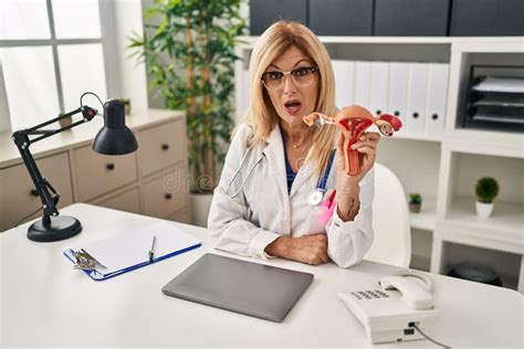 Middle Age Blonde Gynecologist Woman Holding Anatomical Model Of Female Genital Organ Scared And