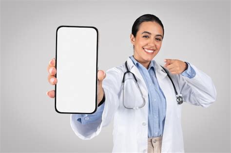 Feliz doctora latina mostrando la pantalla vacía del teléfono celular publicitario del sitio web