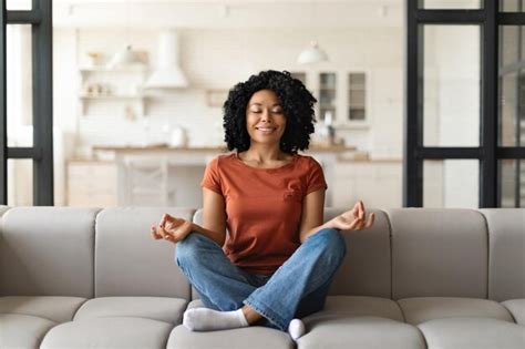 Mujer negra tranquila sentada en el sofá meditando con los ojos