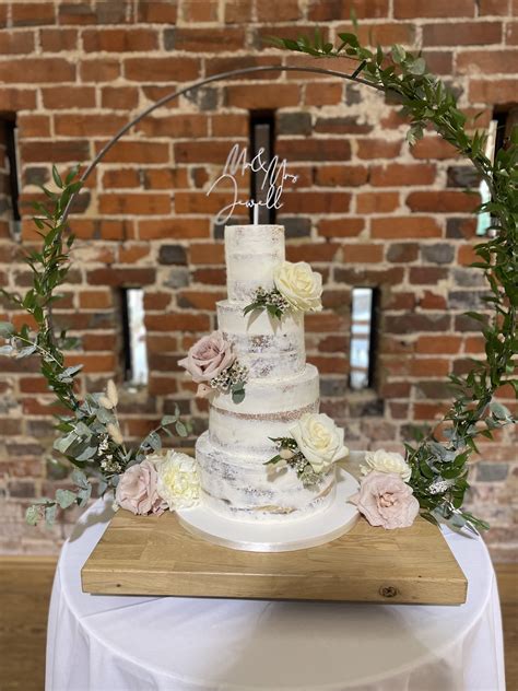 4 Tier Semi Naked Wedding Cake Decorated With Fresh Roses Foliage Displayed On A Hoop Stand