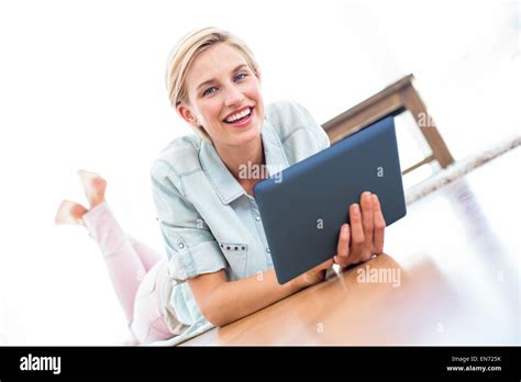 Pretty Blonde Woman Lying On The Floor And Using Her Tablet Stock Photo