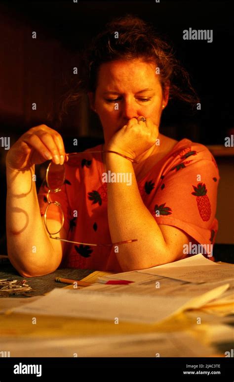 Mature Woman Sitting In Dining Room Beside Stack Of Bills And Shredded
