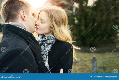 Portrait Of Attractive Blonde Woman In Black Coat Kissing Her Boyfriend With Closed Eyes Stock