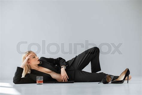 Stylish Half Naked Woman In Black Trendy Suit Lying On Grey With Glass Of Whiskey Stock Image