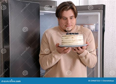 Happy Overweight Man With Cake Near Open Refrigerator In Kitchen Stock