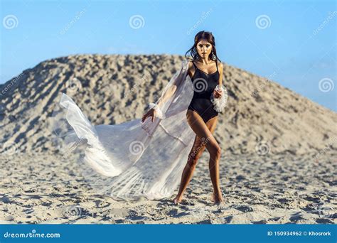 Attractive Brunette Woman In Black Body And Translucent Beach Cover Up Posing On Sandy Beach At