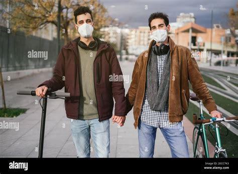 Two Gay Guys Holding Hands While Walking With A Bicycle And An Electric Scooter Looking At The